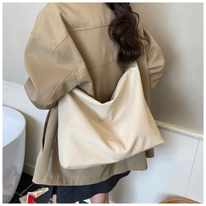 Detail of a large off-white tote bag with pebble leather texture worn by a model