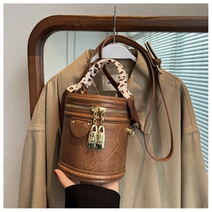 Détail d'un sac cylindrique marron avec foulard léopard et fermeture éclair en métal