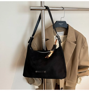 Detail of black suede hobo bag with silver zipper and beaded charm on clothes hanger