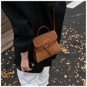 Detail of caramel brown suede crossbody bag with metal buckle on autumn street background
