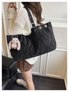 Dettaglio borsa tote nera con texture increspata, occhielli argentati e ciondolo a coniglio