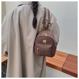 Brown vintage mini backpack with gold zippers shown on model in a warm room setting