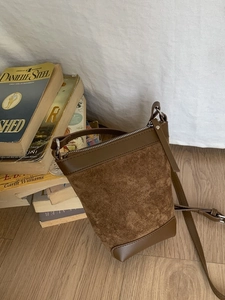 Brown vintage suede bucket bag with adjustable strap and silver zipper on wooden floor