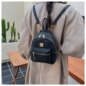 Close-up of a black mini leather backpack worn by a model in an outdoor setting