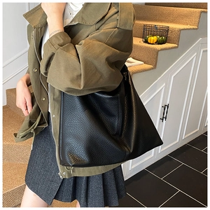 Detailed view of black pebbled leather tote bag worn by a model on a shoulder