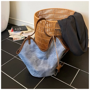 Detail of blue denim tote bag featuring brown leather trim and spacious interior design