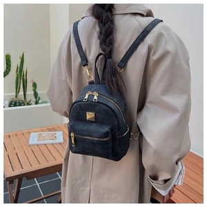Fashionable black mini backpack with golden zippers shown on a model in outdoor setting