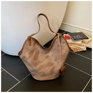 Detail of taupe bucket bag with frosted texture and brown leather trim on floor