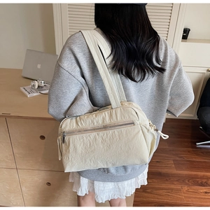 Detailed view of a cream minimalist nylon shoulder bag with front zip pocket and drawstrings