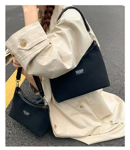 Outdoor shot of a black canvas tote set with metal plate detail on a beige trench coat