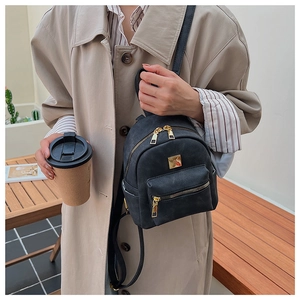 Detailed view of a black mini backpack with golden zippers and matte finish on a model
