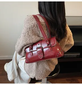 Detail view of deep red vintage shoulder bag with metallic rivets and buckle straps