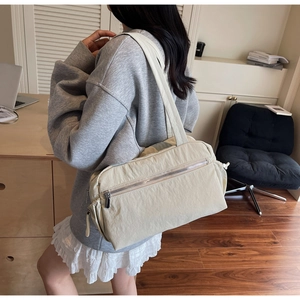 Detail of a minimalist off-white nylon shoulder bag with a functional metal zipper pocket