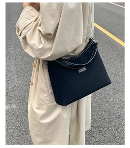 Black canvas underarm bag with leather trim worn with a khaki trench coat outdoors