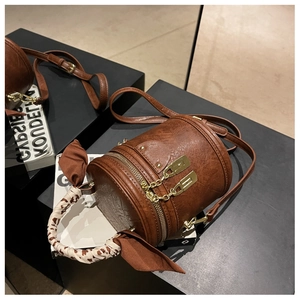 Close-up of brown bucket bag featuring leopard silk scarf handle and golden zippers
