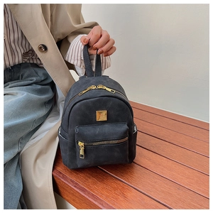 Detail of vintage black mini backpack featuring gold zippers on a wooden bench