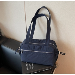 Detail of dark blue nylon tote bag showing front zip pockets and side drawstring accents