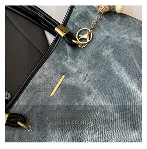 Close-up of grey-blue canvas tote with black leather handle and gold chain detail