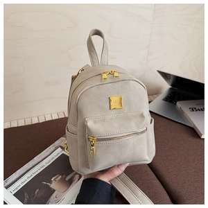 Close-up of the mini beige backpack featuring golden zippers and a square metal logo plate