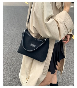 Detail of minimalist black canvas shoulder bag with rectangle label on beige trench coat