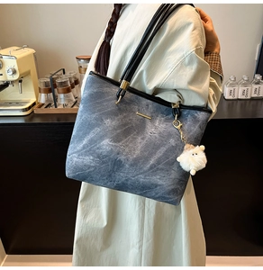 Detail shot of a blue denim tote bag with black straps and a cute white plush lamb pendant