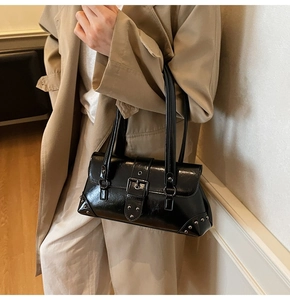 Detail of black glossy vintage shoulder bag with metal buckle on a khaki trench coat