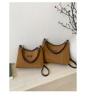 Detail view of two caramel suede underarm bags with leather straps on a stone surface