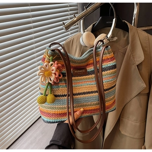 Detailaufnahme einer bunten gestreiften Strohtasche mit Lederriemen und Blumenanhänger