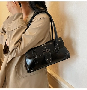 Close-up of black retro motorcycle bag with silver rivets and hardware on a khaki trench coat