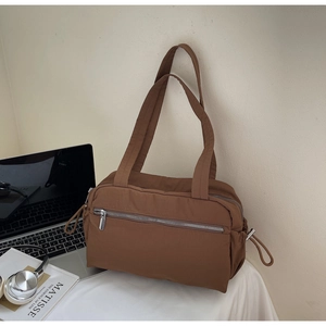 Detail of a brown nylon tote bag with front zipper pocket and side drawstring accents