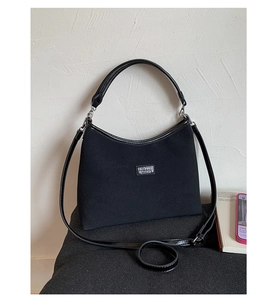 Detail of black canvas tote bag showing silver logo plate and detachable shoulder strap