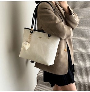 Detail of a large beige leather tote bag with marble texture and plush ball charm