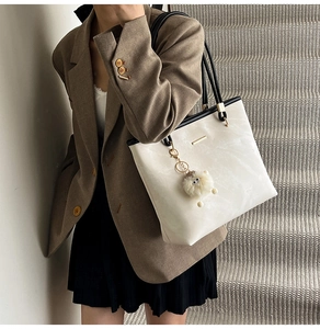 Detail of cream tote bag with black handles and plush pendant on model for daily commute