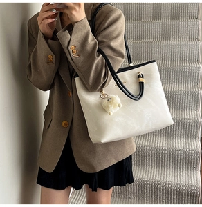 Detail of off-white tote bag with cloud texture, gold hardware, and white plush charm