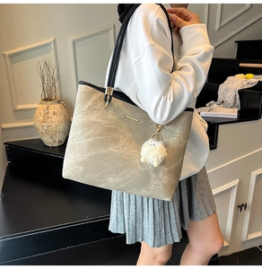 Detail of taupe suede tote bag with black handles and plush charm for daily commute