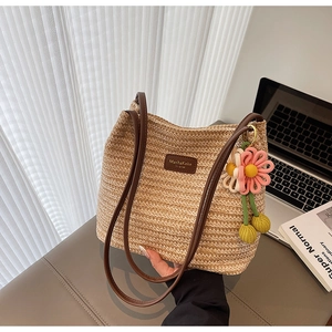 Detail der handgewebten Strohtasche mit Lederlogo und dekorativem Strickblumen-Anhänger