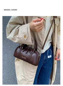 Bolso Boston de cuero marrón oscuro con logo metálico en una toma de moda de estilo calle