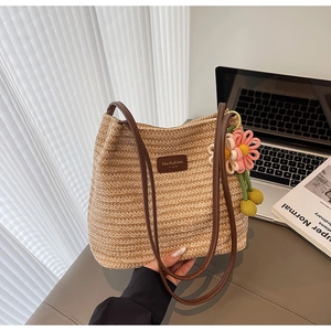 Detail der handgewebten Strohtasche mit braunen Ledergriffen und Strickblumenanhänger