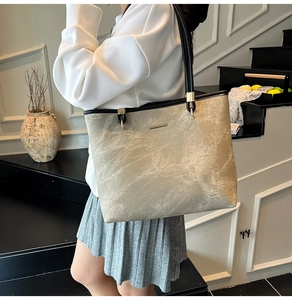 Detail of grey marble pattern tote bag with black leather straps and gold metal accent