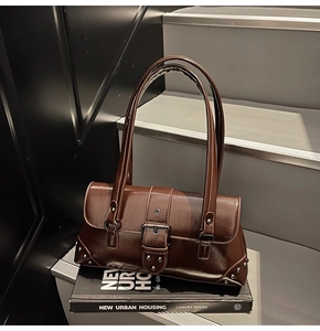 Detail view of brown vintage baguette bag with silver rivets and buckle on a book