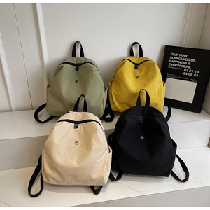 Quattro zaini versatili in nylon verde, giallo, beige e nero su un espositore minimalista