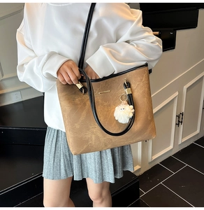 Brown faux leather tote bag with furry pendant shown on a model in a casual indoor setting