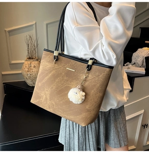 Brown vintage tote bag with black handles and white plush charm on a model's shoulder