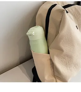 Dettaglio della tasca laterale dello zaino in tela beige con una borraccia verde