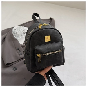 Detail of a mini black matte backpack with gold zippers and multi-pocket design