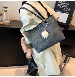 Detail of gray leather tote bag with long black handles and white pom-pom charm
