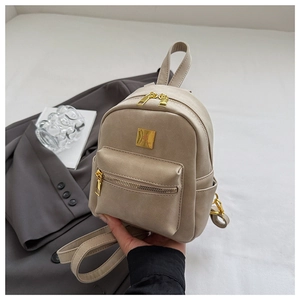 Detail of beige mini backpack featuring golden clover charm and smooth PU texture