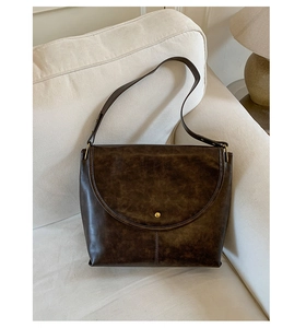 Détail d'un sac à bandoulière vintage marron avec boucle dorée sur un canapé blanc