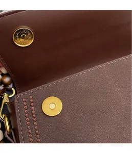 Detail of dark brown leather handbag with gold magnetic closure and wooden beads