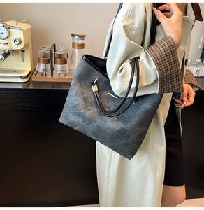 Detail of dark grey tote bag with marble texture leather and gold metal trim